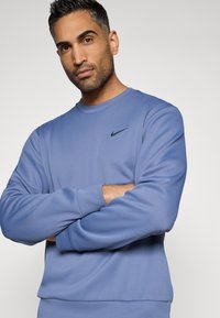 Sweatshirt bleu clair en tissu doux, présentant un col rond et des manches longues. Logo Nike noir sur le côté gauche de la poitrine.
