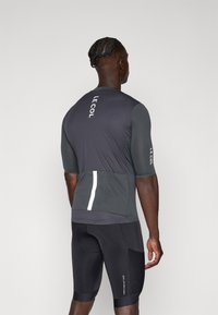 Maillot de cyclisme à manches courtes en gris foncé avec un tissu texturé, des accents réfléchissants et une poche arrière. Assorti à un short rembourré noir.