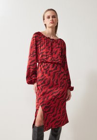 Red dress with black wavy pattern, off-shoulder neckline, long puff sleeves, cinched waist, and thigh-high slit. Smooth fabric texture.