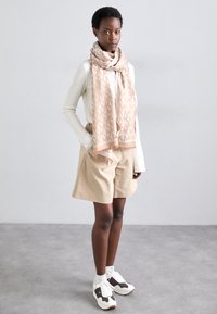 Beige patterned scarf with "MK" design, white ribbed sweater, beige shorts, and white sneakers with brown accents. Smooth texture.