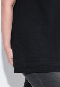 Top nero a maniche corte con vestibilità ampia, caratterizzato da un orlo arrotondato e una texture sottile. Abbinato a leggings grigi aderenti.