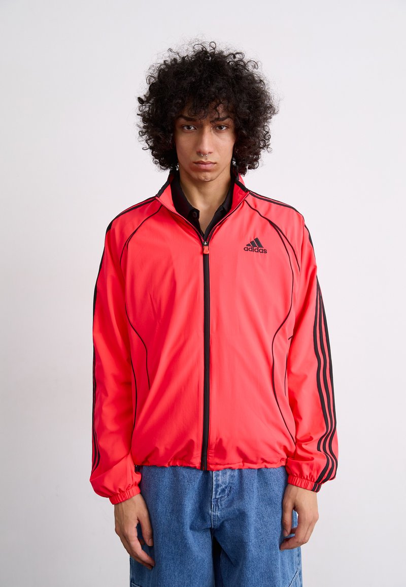 Bright red sports jacket with black accents, zip closure, and elastic cuffs. Features three black stripes along the sleeves. Lightweight fabric.