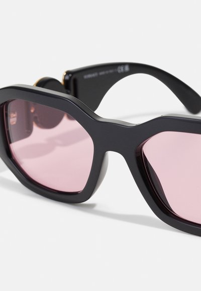 Sorte, oversized solbriller med rosa tonede linser, vinklet design og glat overflade. Har guld hardware accenter på rammes hængsler.