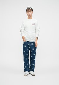 Bela srajca z dolgimi rokavi s tiskanimi grafiki; modri jeans hlače z vzorci yin-yang; bele športne čevlje; minimalni dodatki.