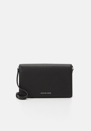 Musta nyppypintainen nahkainen Michael Kors -clutch rannekahvalla ja hopeisella logolla keskellä etupuolta, valkoista taustaa vasten.