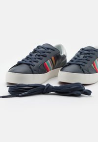 Baskets en cuir bleu marine avec semelles blanches, ornées d'un accent rayé multicolore. Comprend un lacet bleu foncé placé à proximité.