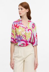 Blusa stampata astratta e colorata con scollatura a V, maniche corte e vestibilità morbida. Il tessuto presenta una miscela di colori rosa, verde e blu.