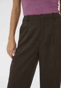 Brown tailored trousers with a high waist, side pockets, and subtle pleats. Material appears smooth with a classic fit.