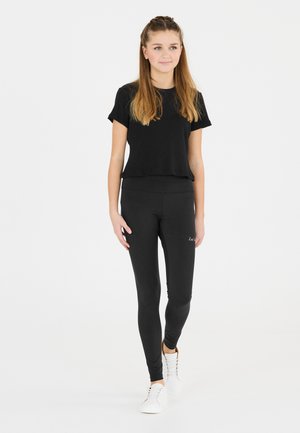 Sort, riflet kortærmet top parret med sorte leggings. Leggingsene har en glat tekstur og en subtil logo-detalje. Hvide sneakers fuldender outfittet.