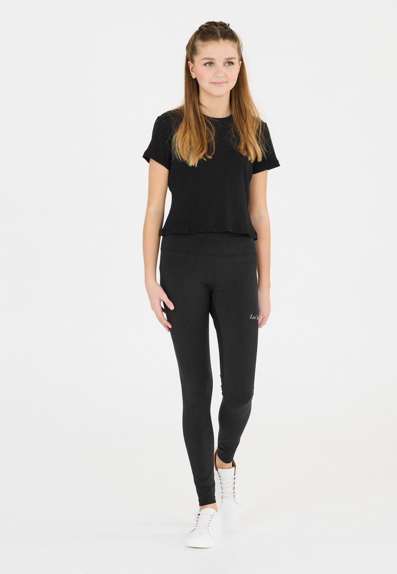 Schwarzes geripptes kurzärmeliges Top, kombiniert mit schwarzen Leggings. Die Leggings haben eine glatte Textur und ein dezentes Logodesign. Weiße Sneakers runden das Outfit ab.