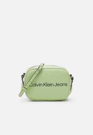 Lysegrøn rektangulær crossbody-taske med justerbar rem, prægede "CK"-logo og teksten "Calvin Klein Jeans" på forsiden.