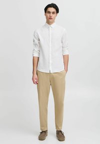 Witte overhemd met lange mouwen, beige taps toelopende broek en bruine suede schoenen. De stof is lichtgewicht met een subtiele textuur.
