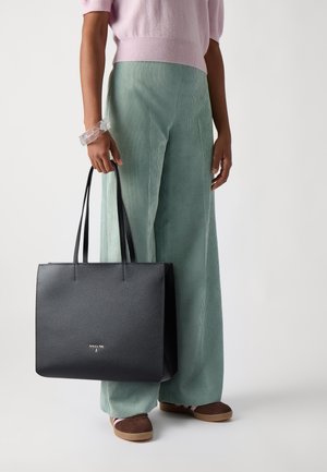 Sac tote en cuir noir avec une forme structurée, texture lisse et doubles poignées supérieures. Logo doré remarquable à l'avant. Accompagné de pantalons en velours côtelé menthe.