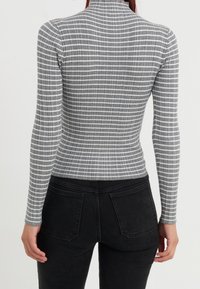 Szary longsleeve z wysokim kołnierzem i prążkowaną teksturą, z poziomymi białymi paskami. Połączony z czarnymi dżinsami.