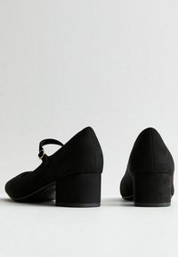 Scarpe nere con tacco a blocco, punta affusolata e una fascia sulla parte anteriore, realizzate in un materiale simile alla suede, con una superficie liscia.