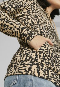 Sudadera con capucha beige con patrón abstracto negro, mangas largas y bolsillo delantero; hecha de material texturizado con capucha ajustable con cordón.