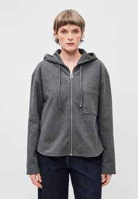 Sivá mikina na zips vyrobená z mäkkého materiálu, s prednou kapsou, kapucňou so sťahovacou šnúrkou a voľným strihom s dlhými rukávmi.