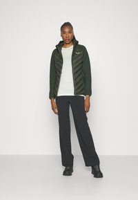 Green quilted jacket with a zip closure, paired with a light gray shirt and black wide-leg pants, featuring a smooth fabric texture.