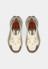 Μπεζ αθλητικά παπούτσια με καφέ λεπτομέρειες, ανώτερο μέρος από δίχτυ, αντιθετικά κορδόνια και υφή στην σόλα. Διαθέτουν επενδεδυμένο γιακά και λεπτομέρεια με λογότυπο.