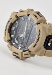 Montre G-SHOCK avec un boîtier en résine beige mat, affichage numérique, accents noirs et boutons surélevés portant les étiquettes "LIGHT", "START", "MODE" et "DISP."