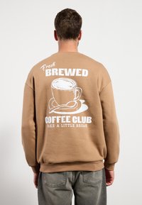 Sudadera marrón con un gran gráfico blanco de una taza de café en la espalda, con el texto: "Fresh Brewed Coffee Club Take A Little Break."
