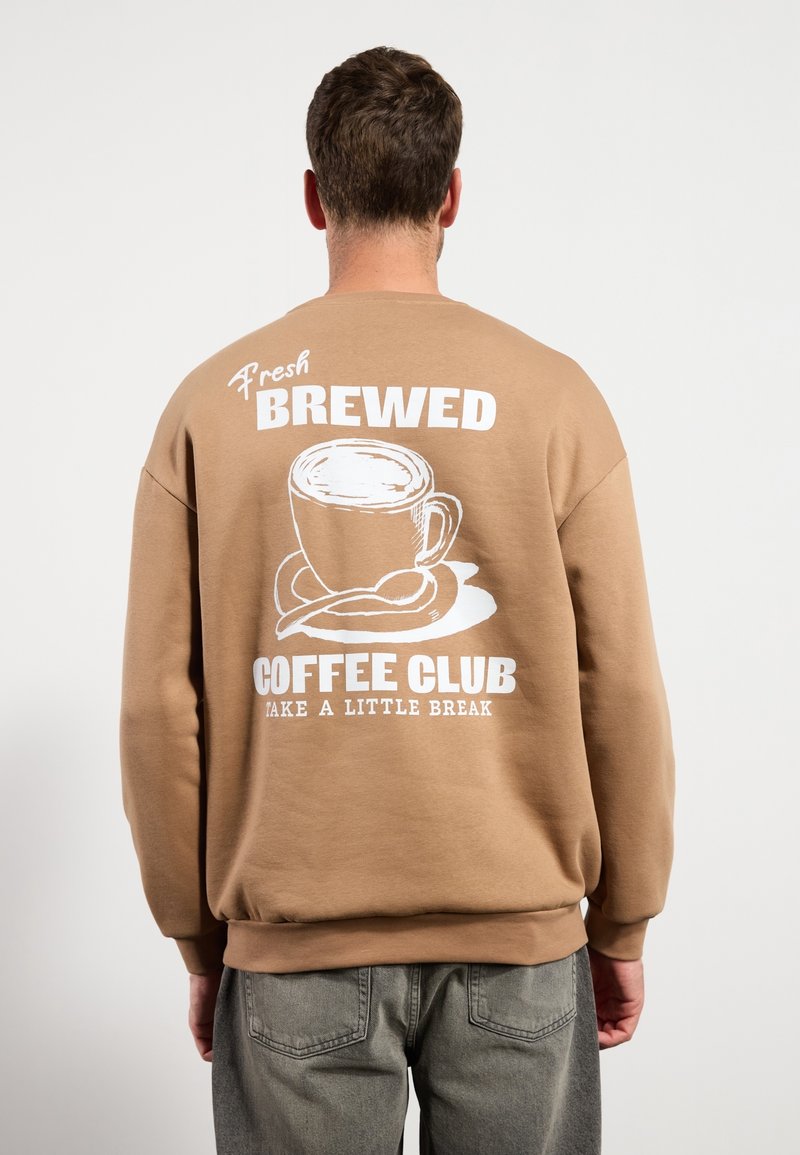 Sudadera marrón con un gran gráfico blanco de una taza de café en la espalda, con el texto: "Fresh Brewed Coffee Club Take A Little Break."