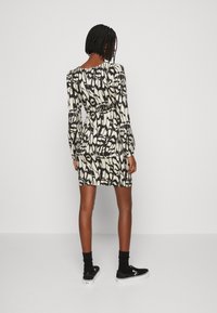 Robe à motifs noir et blanc avec des manches longues, une silhouette ajustée et un col en scoop. Associée à des baskets noires et des chaussettes de cheville.