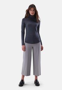 Dunkelgrauer Rollkragenpullover aus einem weichen Stoff, kombiniert mit hellgrauen, weit geschnittenen Hosen und schwarzen Slippern. Glatte Textur, figurbetontes Design.