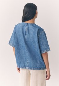 Top in denim a maniche corte con vestibilità ampia, scollo tondo e cuciture a contrasto. Colore: blu medio. Materiale: tessuto denim strutturato.