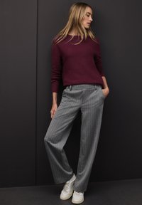 Vinrød sweater med ribbestrikkede ærmegab, kombineret med grå, tyndstribede bukser med vide ben. Hvide sneakers fuldender outfittet.