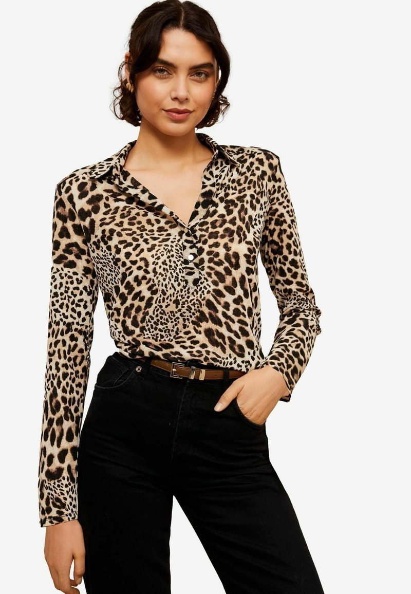 Blusa a maniche lunghe con print leopardato in tonalità beige e nero. Presenta un colletto e tre bottoni sul petto. Abbinata a pantaloni neri.