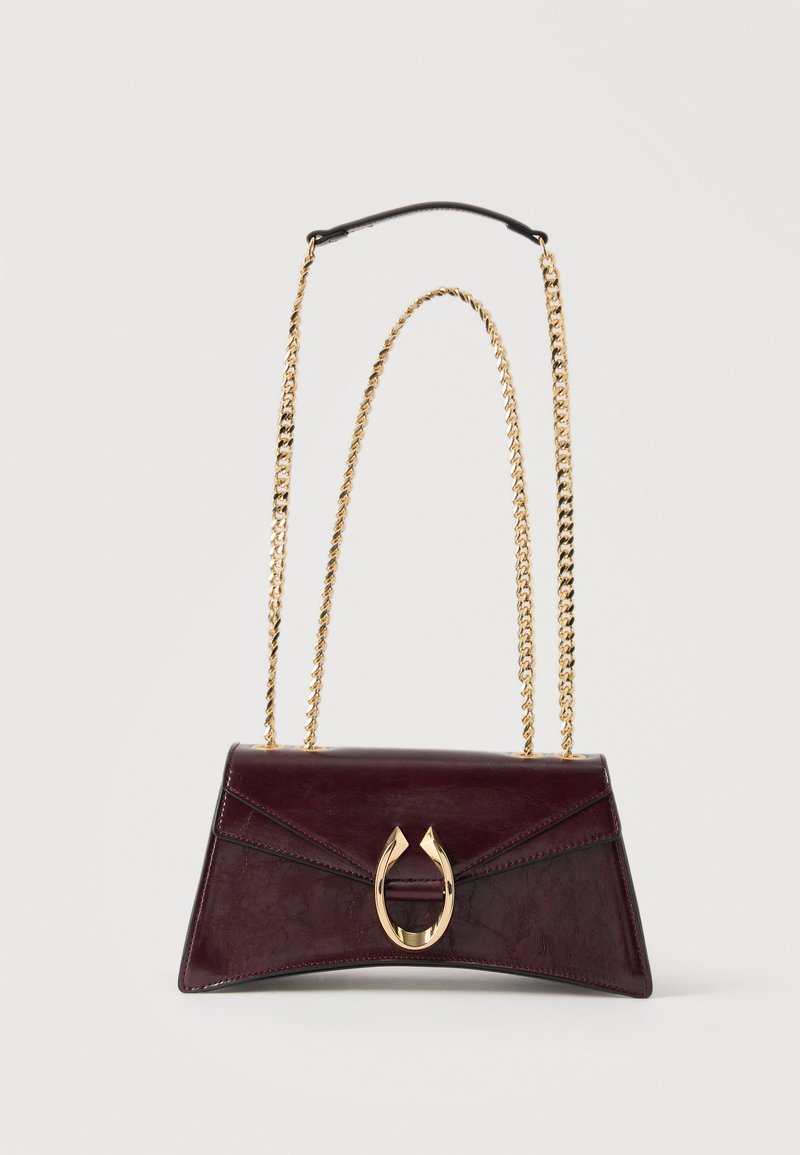 Tumši vīnsarkanās ādas soma ar zelta pakavas aizdari un diviem zelta ķēdes siksnām uz vienkārša balta fona.