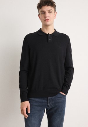 Zwarte lange mouwen polo trui met een kraag, voorzien van twee knopen, een geribde zoom en een subtiele logo op de linkerborst. Draag het met een blauwe jeans.