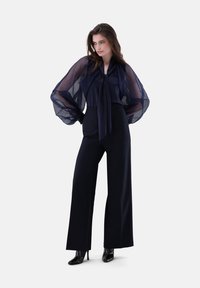 Blusa blu navy con maniche trasparenti e fluide e fiocco. Abbinata a pantaloni neri a vita alta, sartoriali e tacchi neri lucidi.