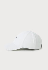 White cap with a curved brim, single black logo detail on front, six-panel design, and adjustable strap at the back. Soft material texture.