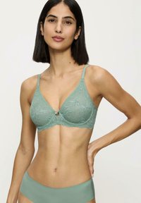 Reggiseno sotto rete verde chiaro con motivo floreale, spalline regolabili e un piccolo elemento decorativo centrale. Tessuto morbido e trasparente.