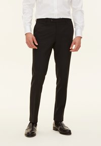 Pantaloni neri su misura con una texture liscia, vestibilità slim e design a vita piatta, abbinati a mocassini neri lucidi.