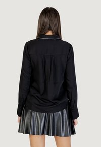 Camicia nera a maniche lunghe con colletto, pieghe sul retro, abbinata a una gonna svasata nera in ecopelle. Texture liscia, design minimalista.