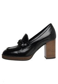 Mocasines de charol negro con tacón alto y decorativo borlas en la parte delantera, con un tacón cuadrado de textura similar a la madera.