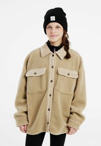 Veste en laine polaire beige avec col en velours côtel�é, deux poches avant et fermeture boutonnée. Accompagnée d'un bonnet en tricot noir avec un patch logo.