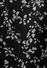 Tissu noir avec un motif floral abstrait blanc composé de formes irrégulières de tailles variées, créant une apparence texturée.