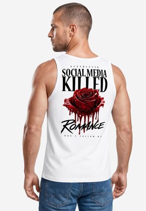 Mann in weißem Tanktop mit Text "Social Media Killed Romance" und rotem Rosenmotiv, das auf dem Rücken Flüssigkeit tropft, trägt blaue Jeans.