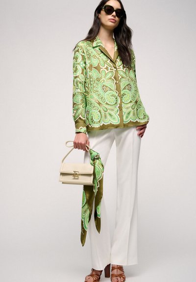Blouse en soie à motifs verts et olive, pantalon blanc à jambes larges, sac beiges avec une écharpe et lunettes de soleil. Texture lisse, design audacieux.