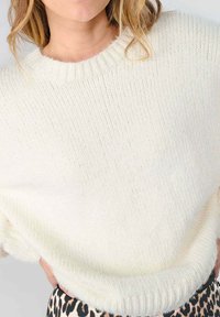 Off-white gebreide trui met een geribbelde textuur, brede halslijn en verlaagde schouders, gecombineerd met een gemusterde rok.
