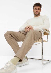 Beige wolmix broek met een rechte pasvorm, gecombineerd met een crèmekleurige geribbelde trui en lichtbeige sneakers. Moderne chroomstoel.