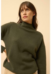Maglione lavorato a maglia verde oliva con collo alto, vestibilità comoda e polsini a coste. Texture morbida con una silhouette leggermente rilassata.