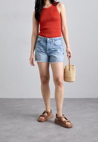 Red ribbed tank top, light blue denim shorts with frayed hem, brown sporty sandals, and a woven straw bag. Simple and casual outfit.