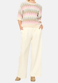 Stickad tröja med flerfärgad zigzag-mönster i pastellfärger, vida ärmar, i kombination med krämfärgade vida byxor och bruna ankelstövlar.