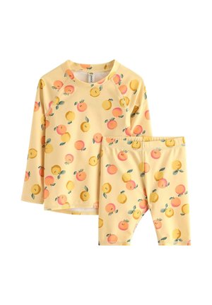 Set composto da top a maniche lunghe e pantaloncini gialli con motivi di frutta arancione e gialla e foglie verdi su sfondo bianco.