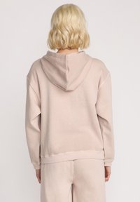 Lys beige hoodie med en løs pasform, stor hætte og ribbede manchetter. Blød tekstur, synlige sømme, båret med matchende bukser.